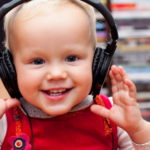 a photo of a blonde toddler with light skin wearing headphones and smiling