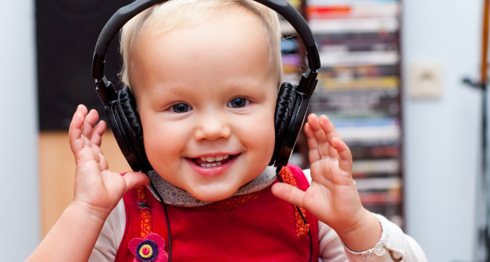 a photo of a blonde toddler with light skin wearing headphones and smiling