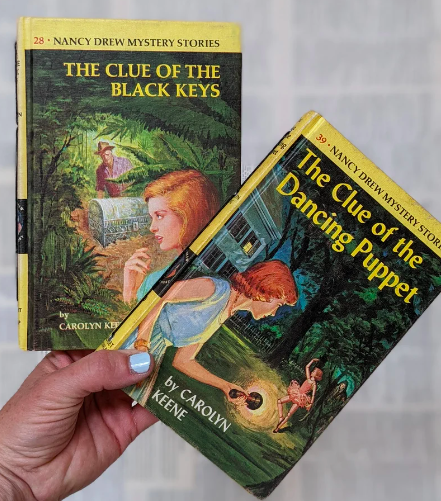 A hand holding two vintage Nancy Drew books that have been emptied and refilled with blank notebook paper