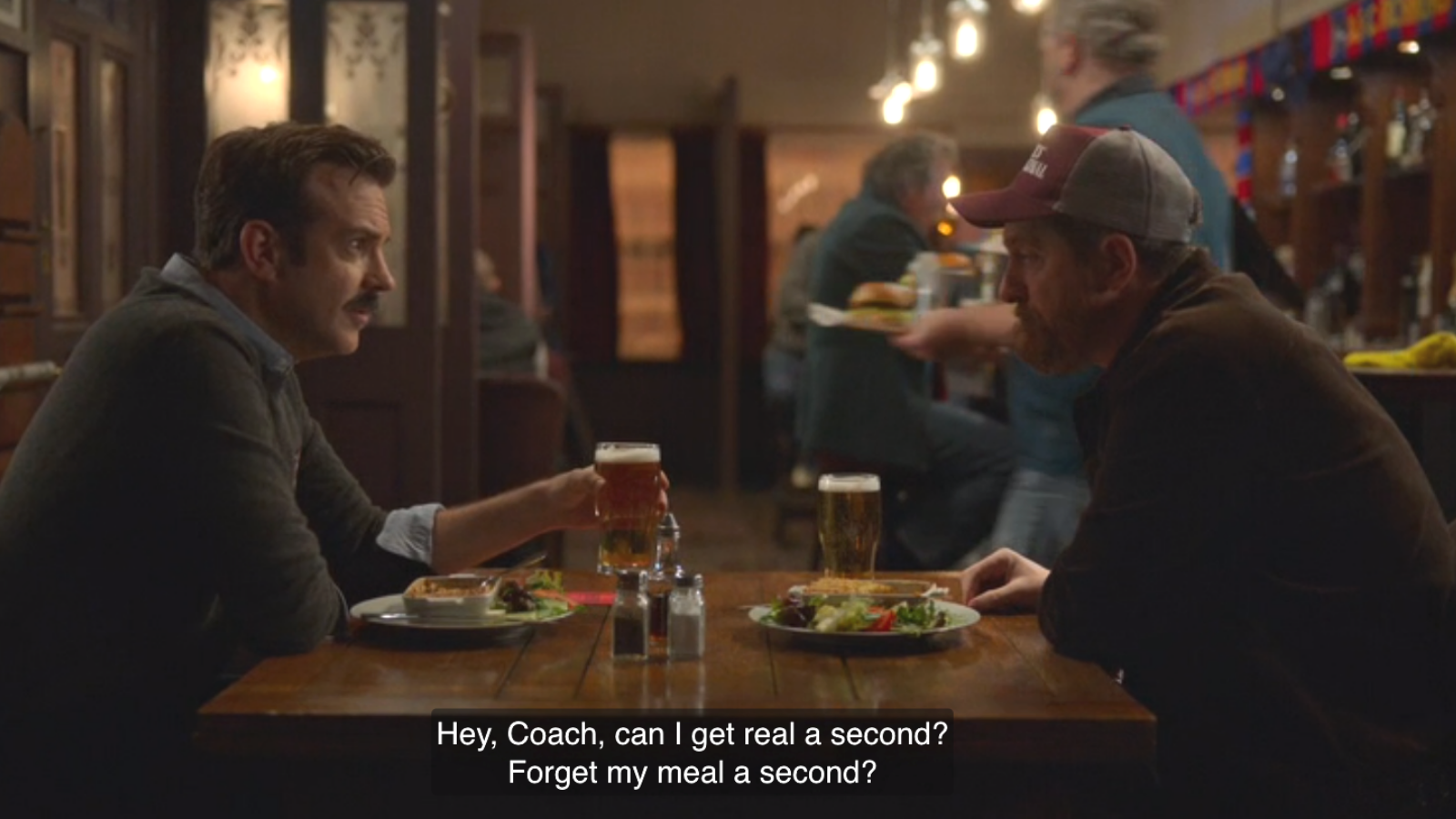 a still of Ted and Beard in a bar. Ted says, "Hey Coach, can I get real a second? Forget my meal a second?"
