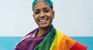 tan-skinned woman with short hair smiling while wrapped in queer pride rainbow flag