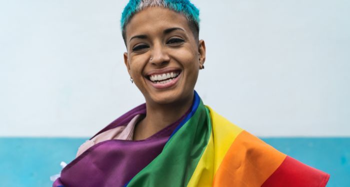 tan-skinned woman with short hair smiling while wrapped in queer pride rainbow flag
