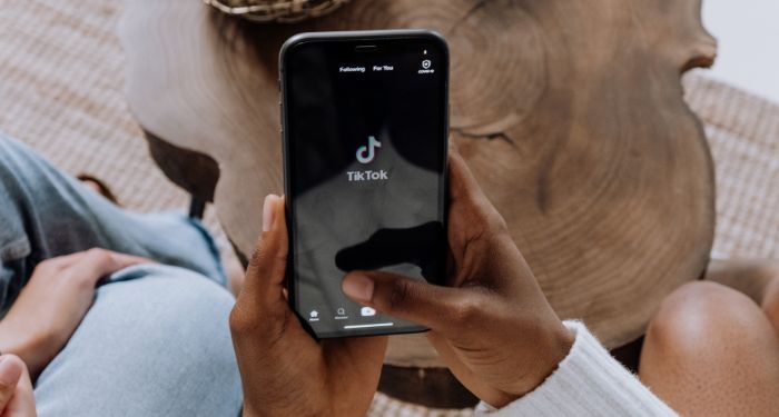 brown-skinned hands are holding a phone with TIkTok on the screen