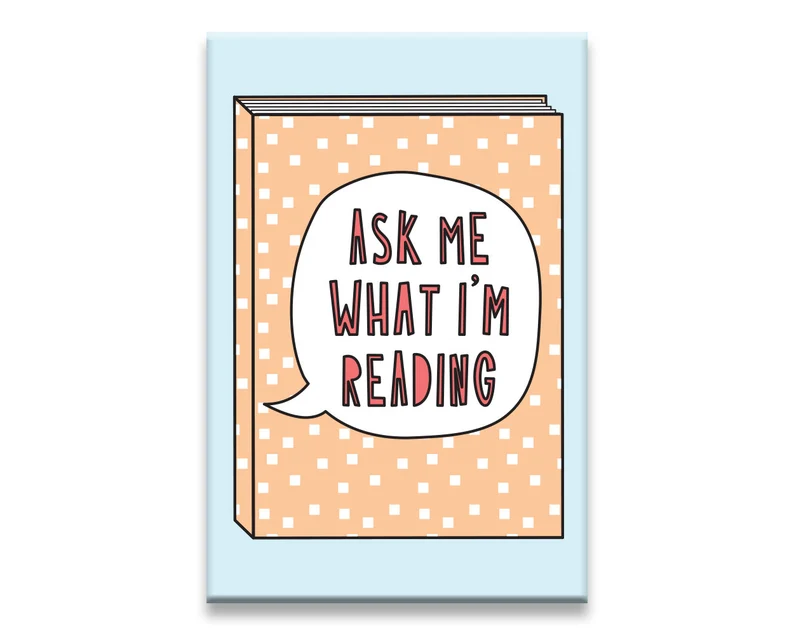 Image of a magnet that is blue with a peach colored book. The book has a text bubble which reads "ask me what I'm reading" in pink. 