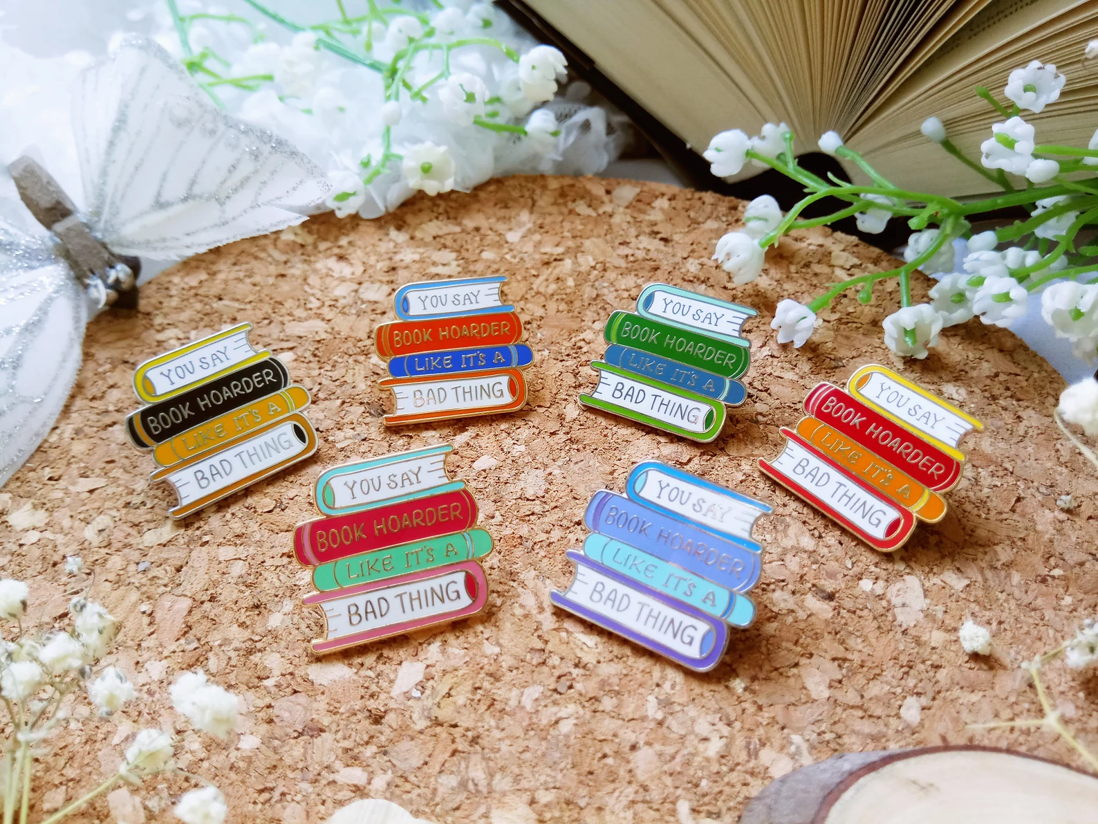 Enamel pins depicting stacks of books with the words "You say book boarding like it's a bad thing"