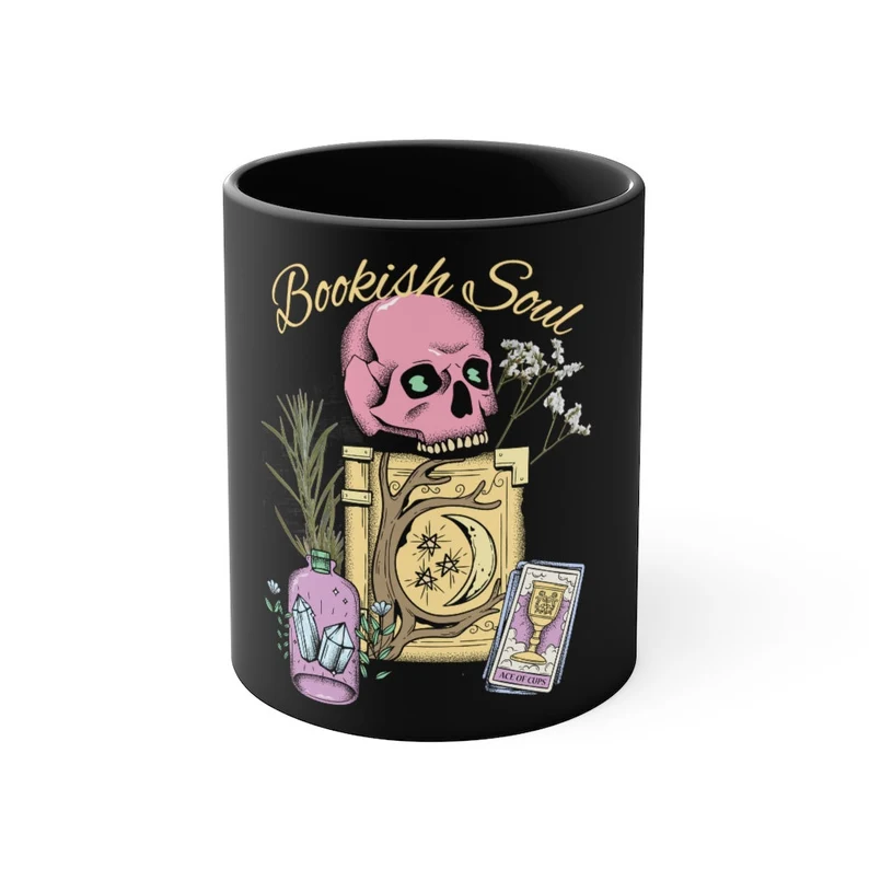 Image of a black mug with a pink skull, purple bottle, and yellow grimoire image. It reads "bookish soul."