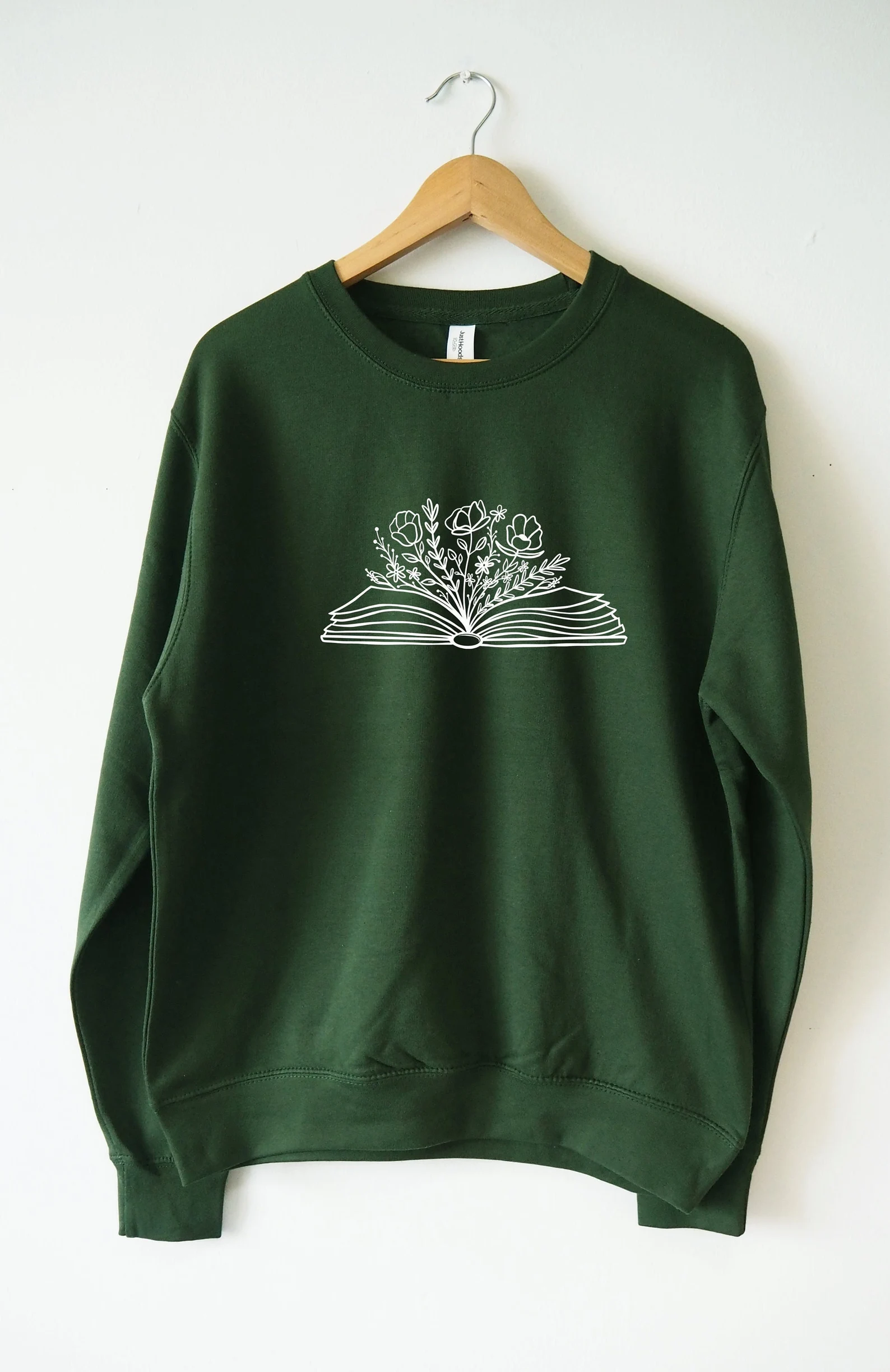 A long-sleeved green shirt printed with a small illustration of an open book overflowing with flowers.