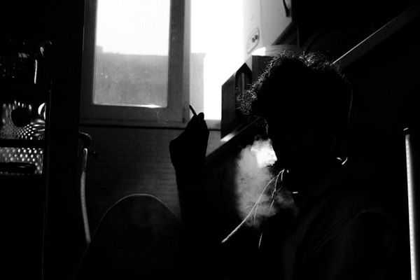 black and white photo of someone smoking  on the floor of a kitchen