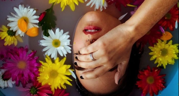 light-skinned woman floating in a bathtub with water and flowers