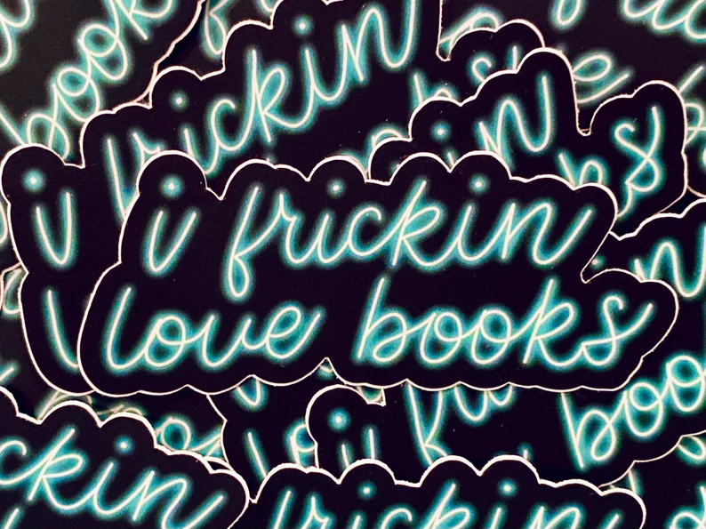 Image of a stack of magnets. They are black with neon blue letters. The words say "I Frickin Love Books."