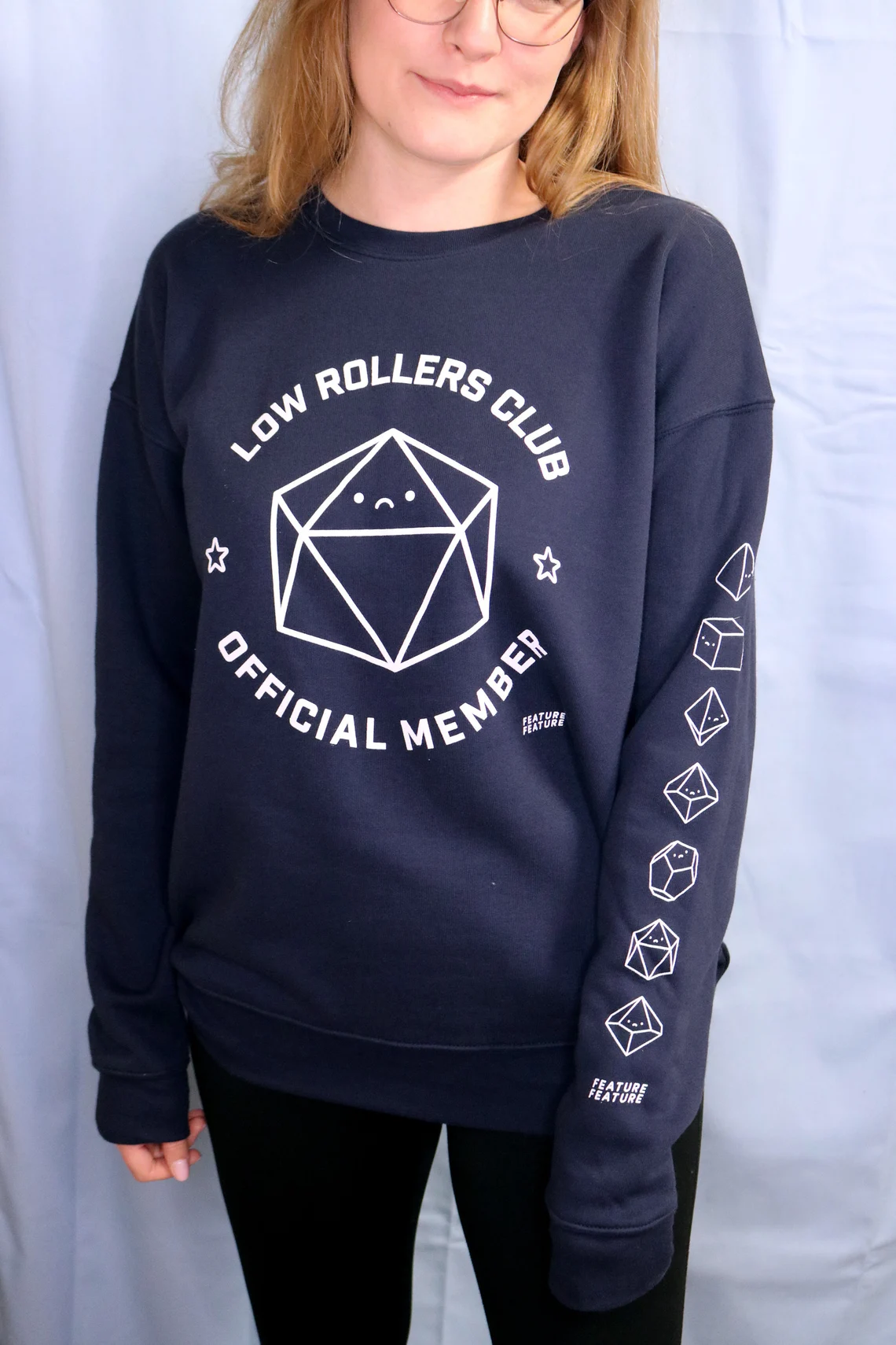 photo of a person wearing a grey shirt with an illustration of sad dice on the front and down the left sleeve. around the dice on the front is the text, "low rollers club official member"