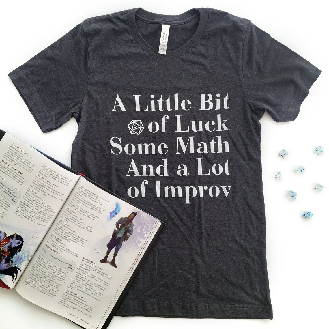 photo of a grey shirt with the text "A Little bit of Luck, Some Math, and a Lot of Improv" written on it with an illustration of a D20 with the "20" facing out