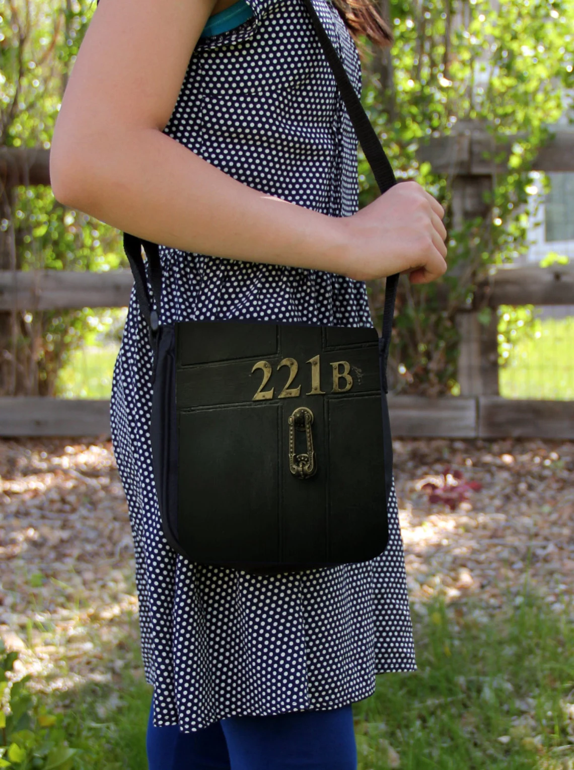 photo of a person in a polka-dot dress wearing a black messenger bag styled like a door with the 221 B door number on it 
