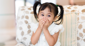 a photo of a kid with pigtails covering her mouth with her hands