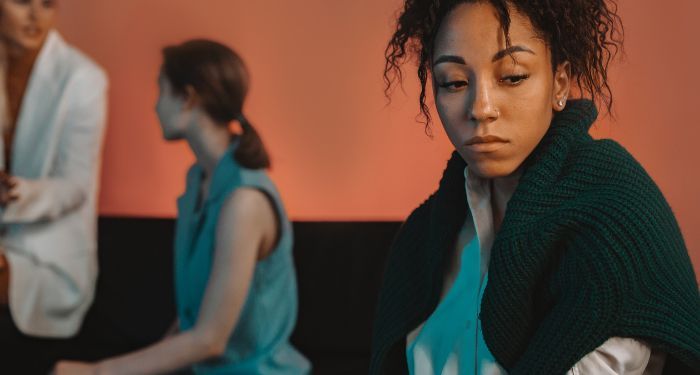 a Black woman looking isolated while two white women speaking to one another in the background