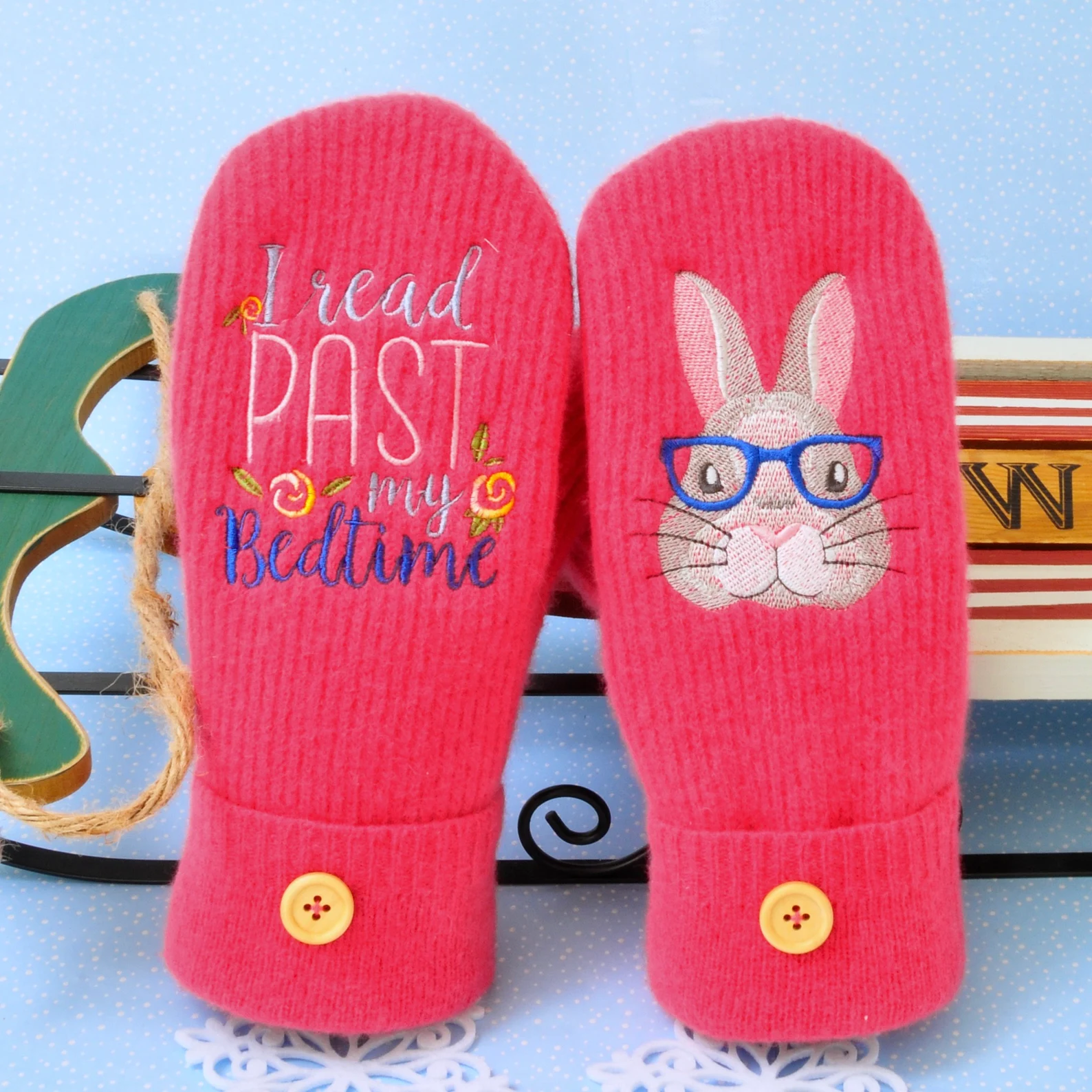 A pair of pink wool mittens. One says "I read past my bedtime" and the other has a picture of a rabbit wearing glasses.