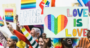a photo of a Pride event, with people holding signs with rainbows on them saying Love is Love