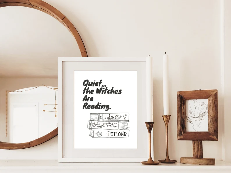 Image of a print on a mantle. The print is black and white. It has a stack of books and says "quiet...the witches are reading."