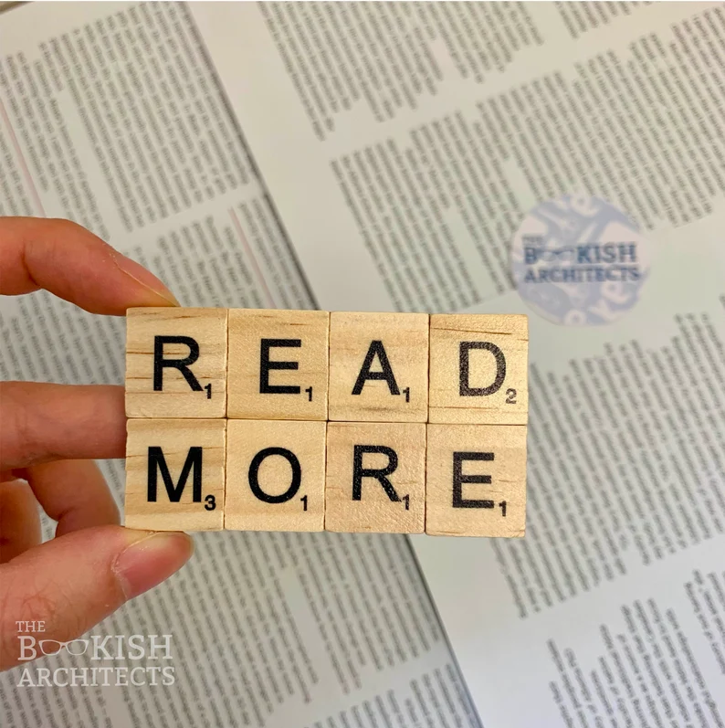 Scrabble tiles turned into a magnet. The magnet reads "Read More" in two rows. It is held by a light colored hand. 