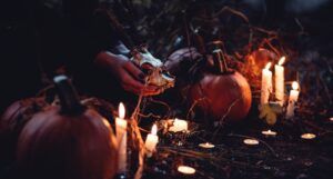 hands holding an animal skull in a dark space filled with candles and pumpkins