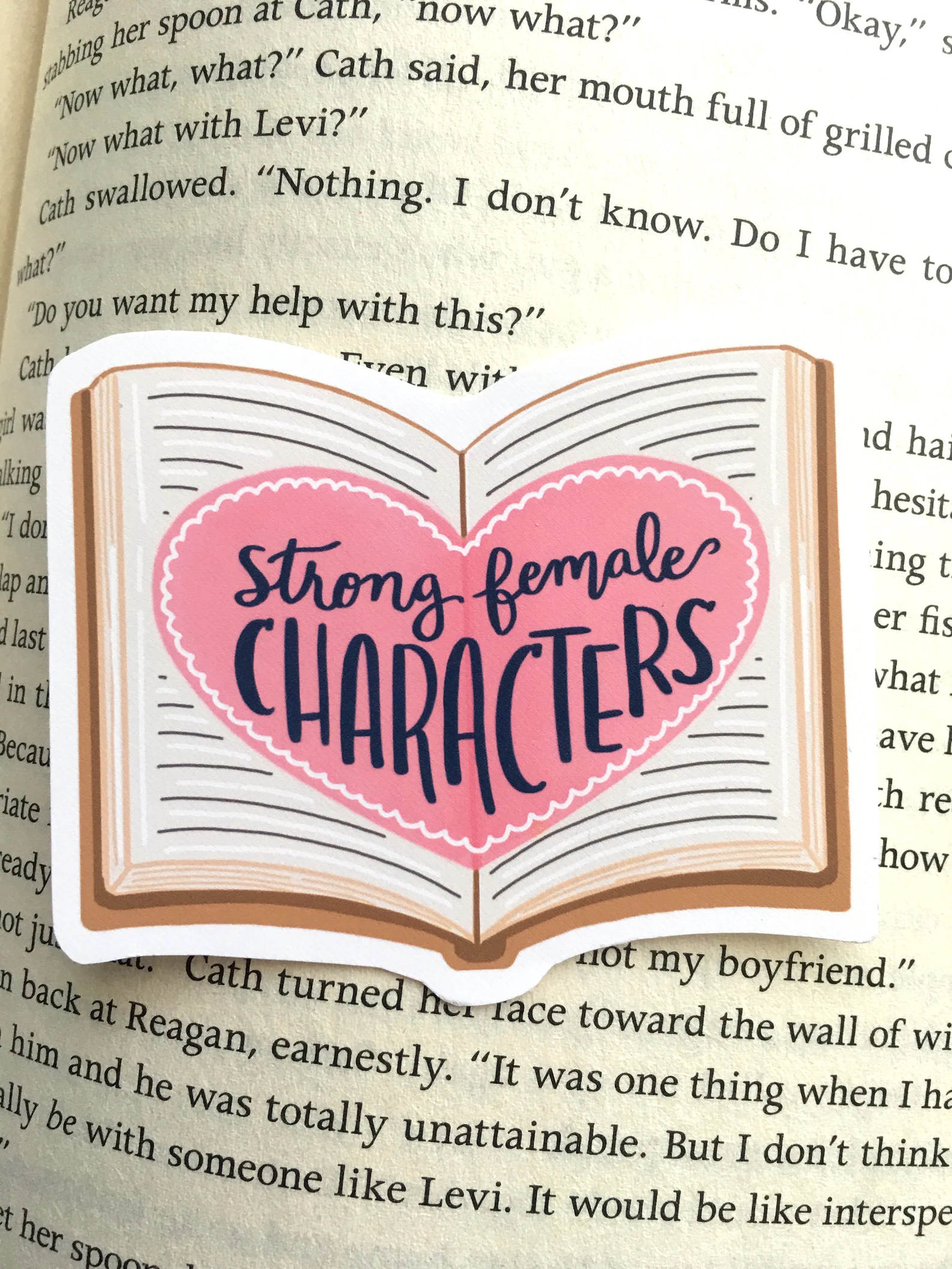 A sticker of an open book with a heart inside that reads "Strong female characters"