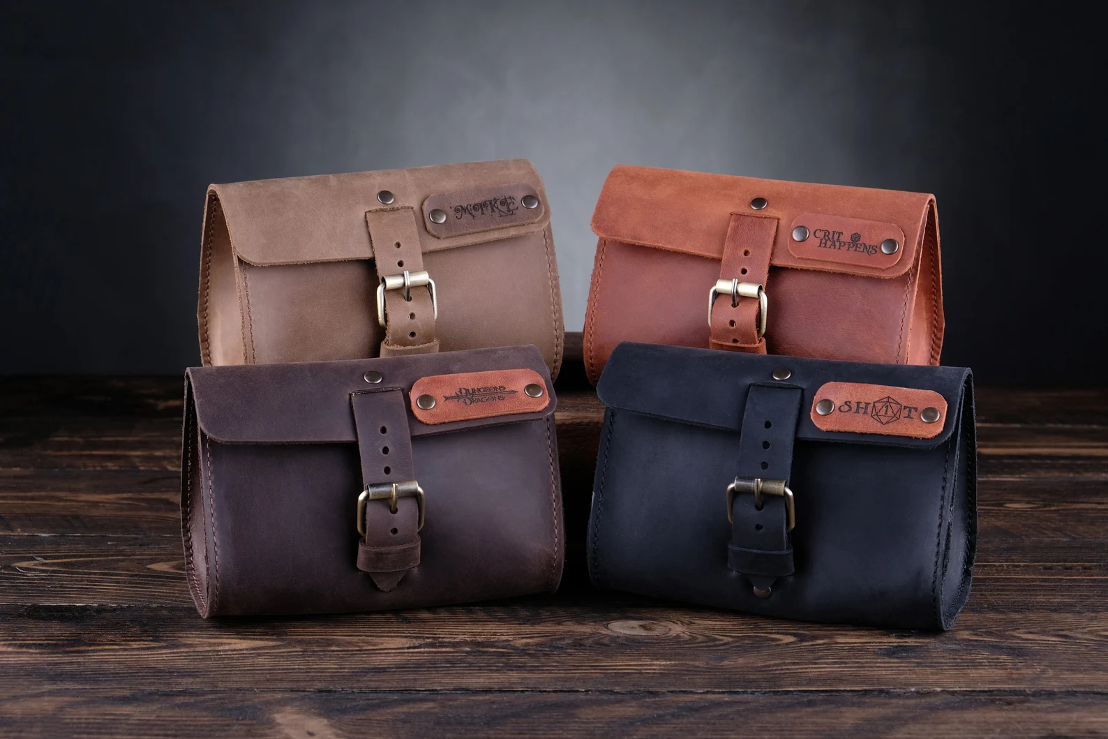 A photo of a gray leather bag, a light brown leather bag, a dark brown leather bag, and a black leather bag. Each bag has a personalized nameplate and a silver buckle on the front. 