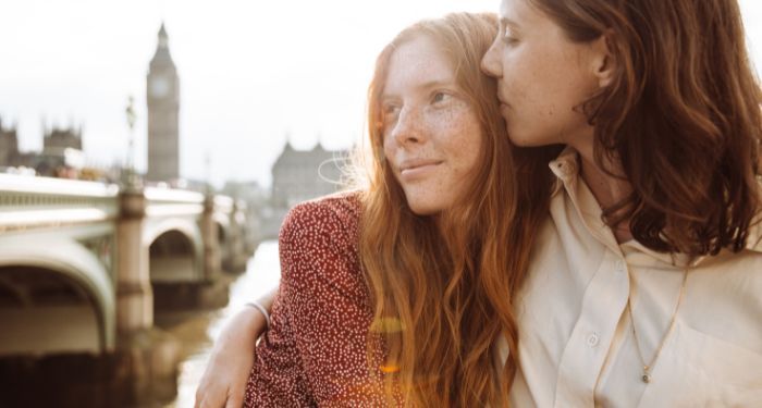 two light-skinned women embracing each other romantically iwith Big Ben and Westminster bridge in the background