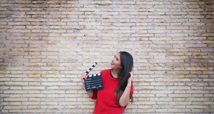 light-skinned woman with a clapboard for movies standing in front of a brick wall