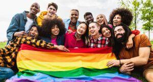 people of different skin tones on the grass smiling and holding the Pride flag