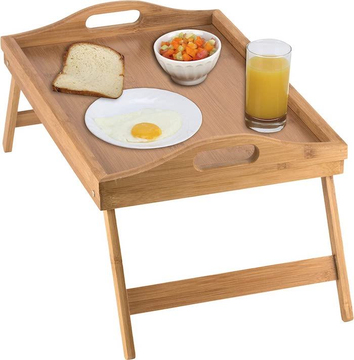 a wood tray table with juice and breakfast foods on top