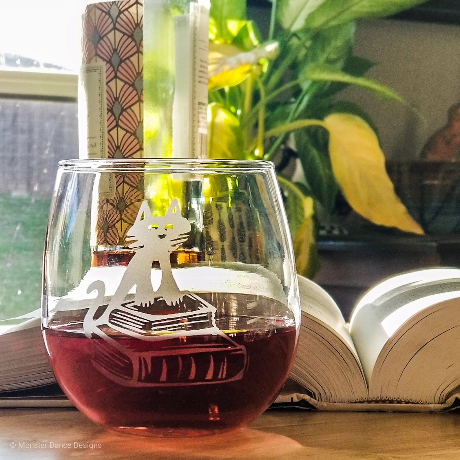 Image of a stemless wine glass with an image of a cat on a stack of books.