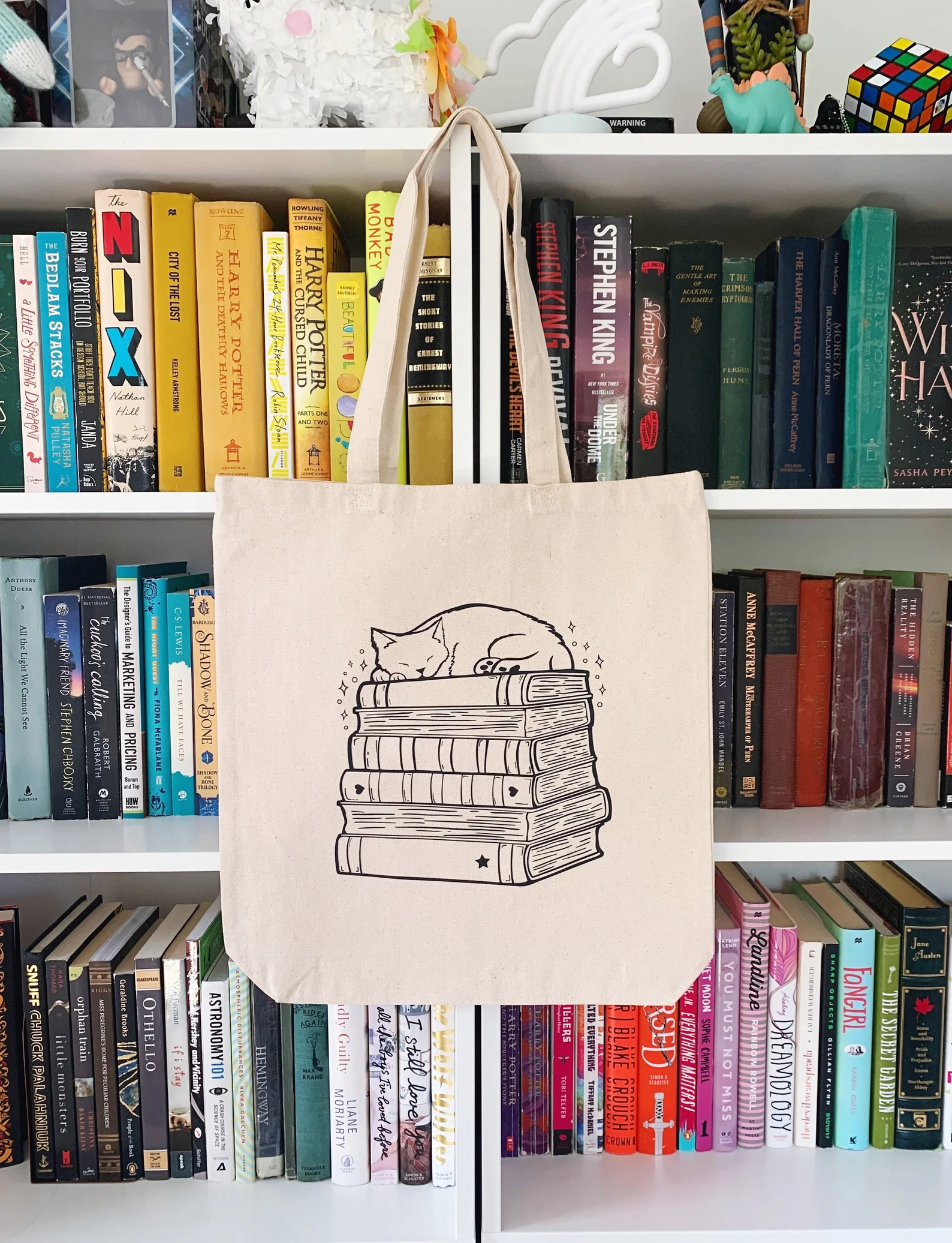 Image of a canvas tote bag with an image of a cat on top of a book stack.