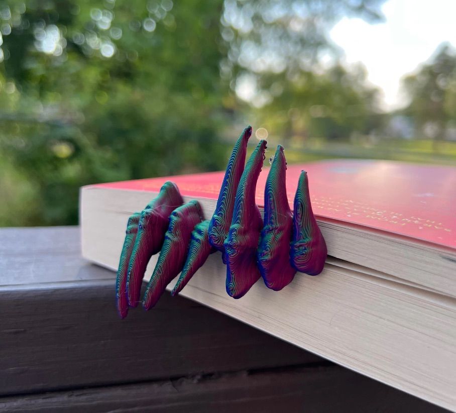Image of a bookmark inside of a book that looks like a set of hands coming out of the book's edge. 