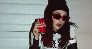 light-skinned girl with red lipstick, a beanie, holding a red can of coke
