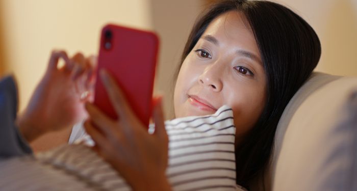 Image of an Asian woman reading on her phone in bed