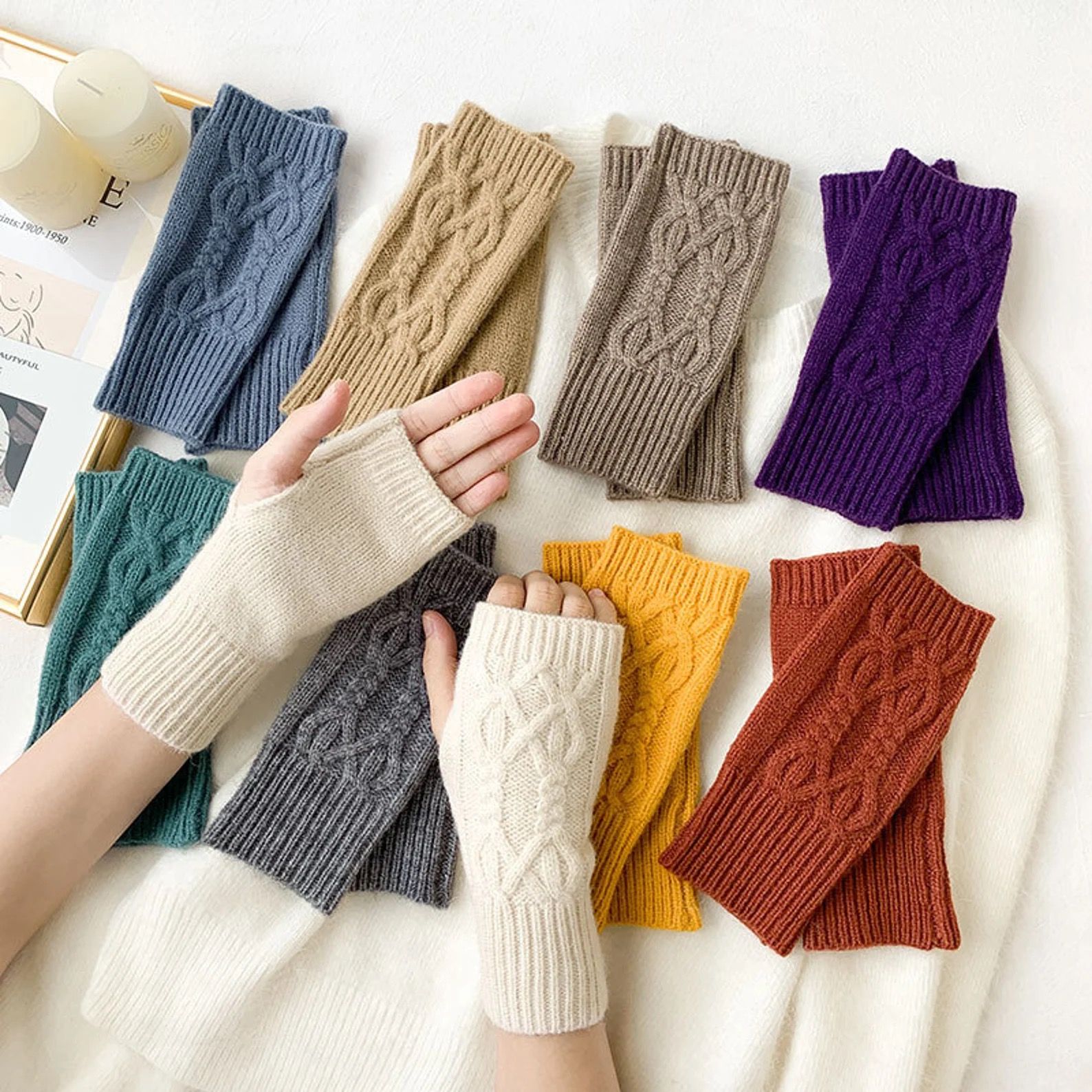 a pair of hands wearing a cream pair of knit fingers gloves, positioned over eight pairs of fingerless gloves in assorted colors