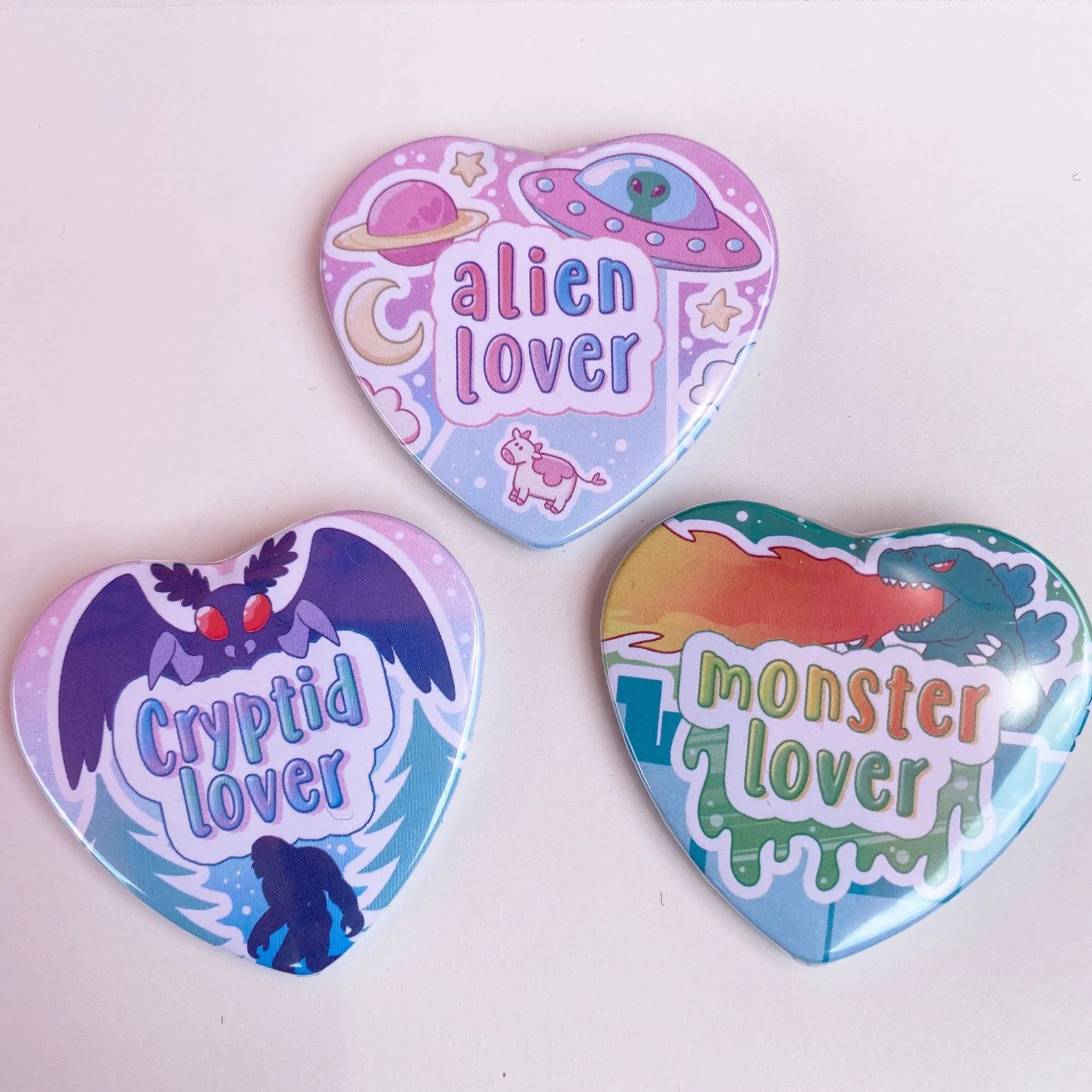 heart-shaped pins reading alien lover, monster lover, and cryptid lover