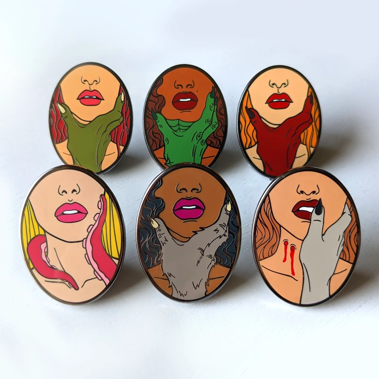 oval pins with women being held by various monsters