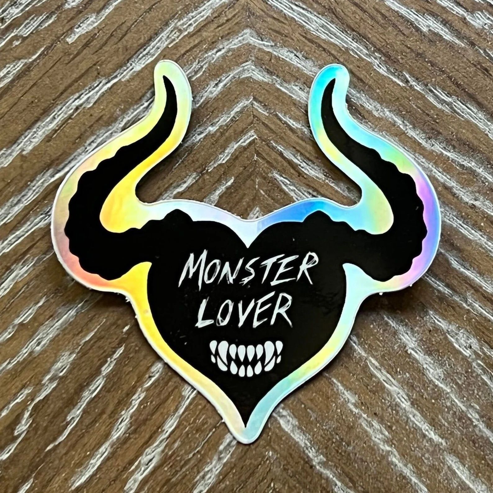 holographic sticker saying monster lover. Heart-shaped with horns and teeth.
