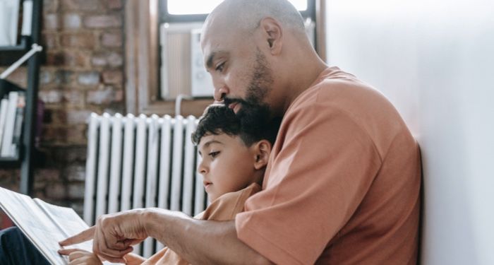 a father reading a picture book to their child seated in their lap