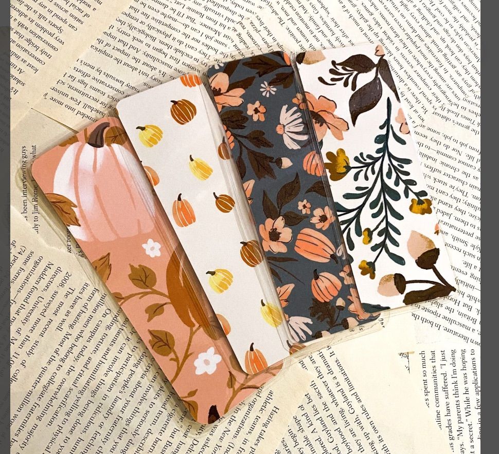 four bookmarks featuring pumpkins, acorns, and other fall foliage on a book page background. 