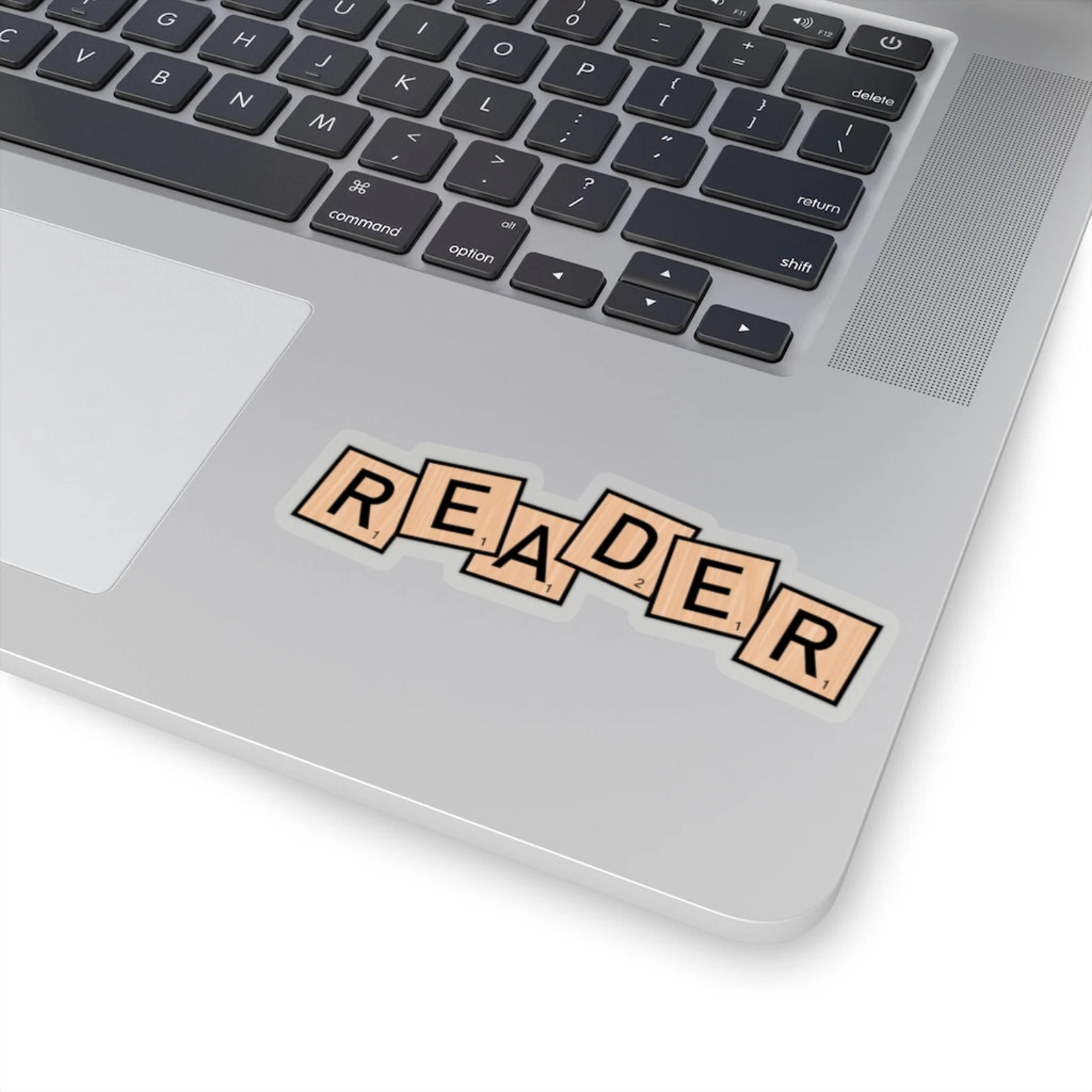 Image of a sticker with scrabble inspired tiles that says "reader." It is on a laptop. 