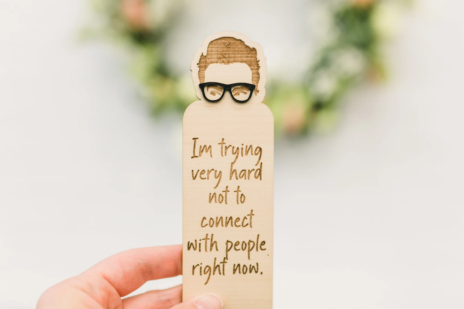 A wooden bookmark with the outline of David Rose's face and the quote "I am trying very hard not to connect with people right now."