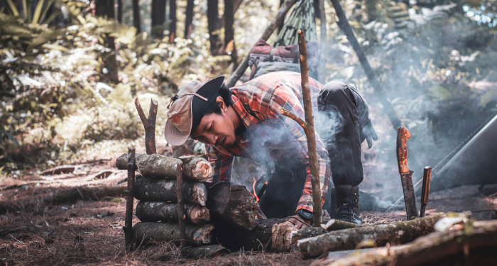 a photo of a man starting a campfire in the woods