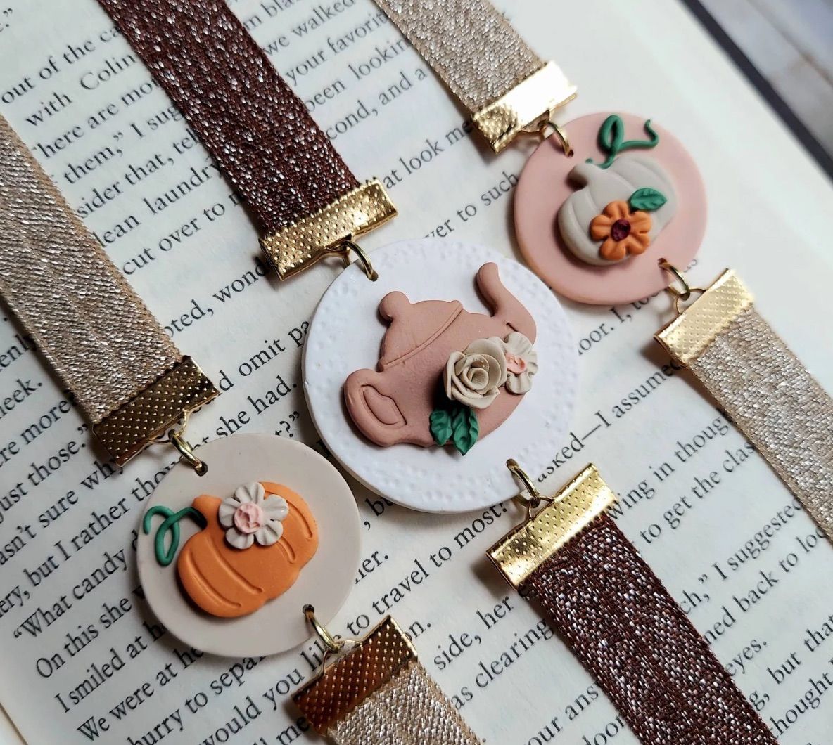 Image of three stretchy bookmarks. Two include pumpkins and one is a tea pot. All are in fall colors and the designs are made from clay. 