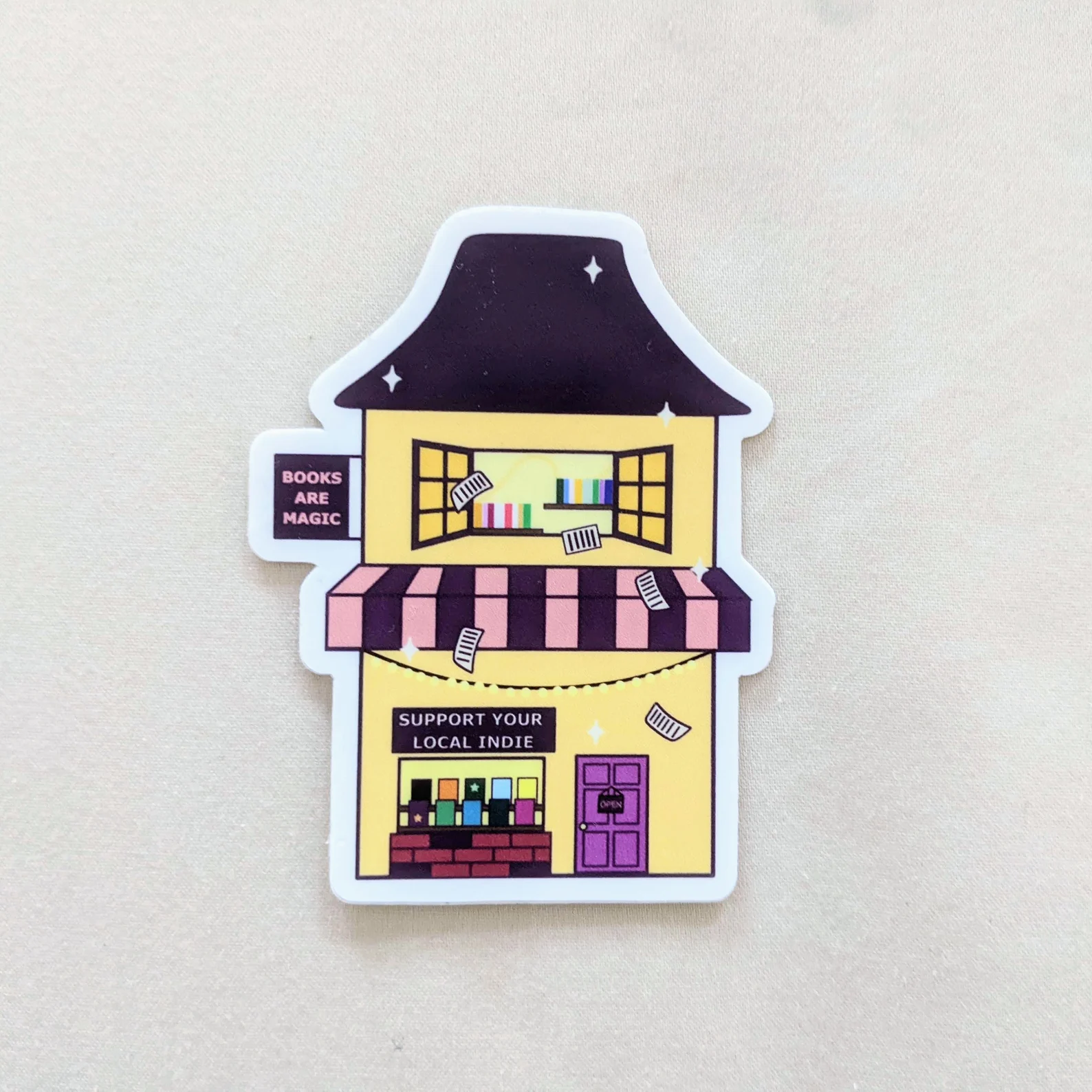 Image of a colorful bookstore sticker. It has a sign that says "books are magic," and a sign that says "support your local indie." 