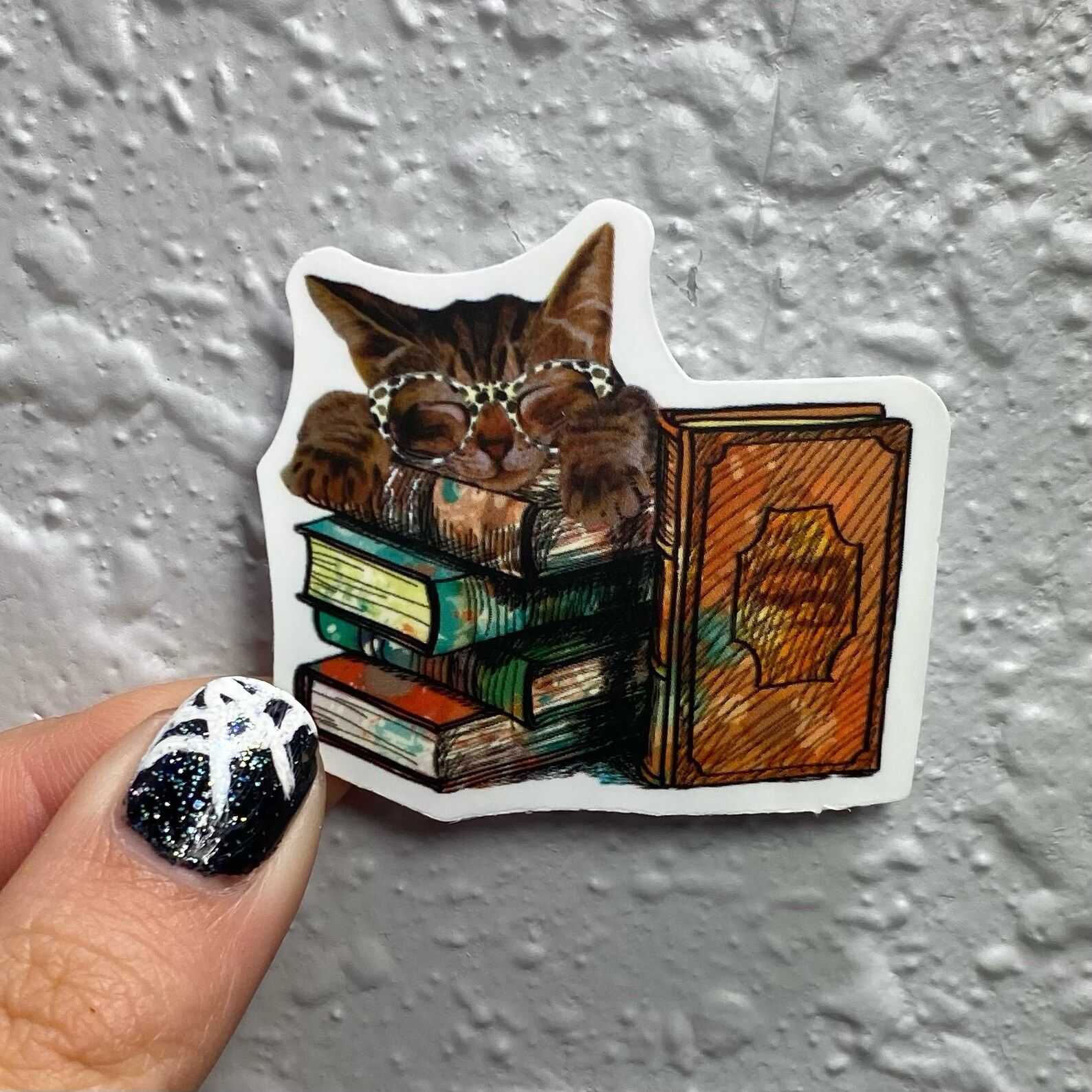 Image of a vinyl sticker featuring a tabby cat in glasses on top of a stack of books.