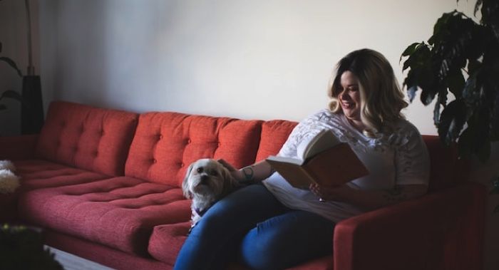 White plus size woman smiling while reading on couch with dog