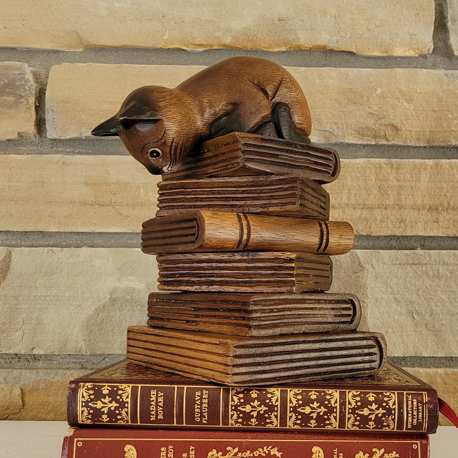 Image of a wooden piece of art featuring a cat on a book stack. 