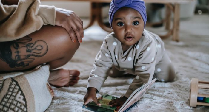 cute Black baby girl with big, brown eyes and her mother's leg Ito the left of the picture